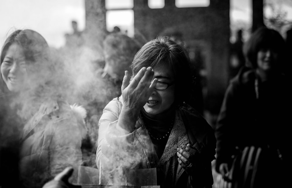 grayscale photography of woman covering her face from smoke