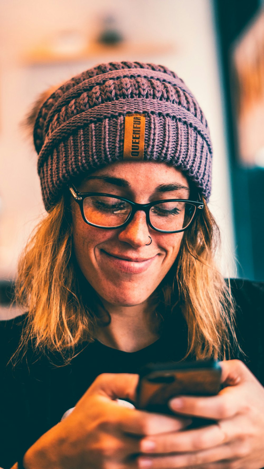 woman wearing black framed eyeglasses and grey knit beanie while using smartphone