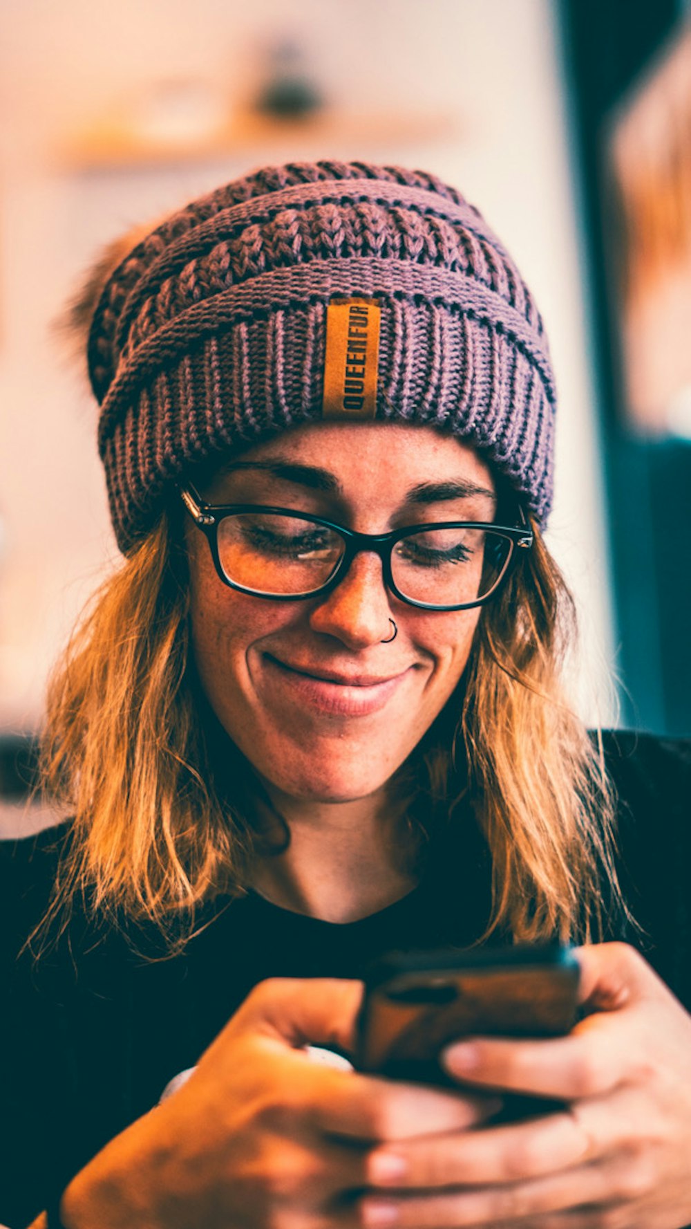 femme portant des lunettes à monture noire et un bonnet en tricot gris tout en utilisant un smartphone