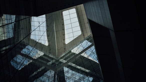 A geometric and architectural view of a building's interior emphasizing a large skylight. The scene is characterized by reflective surfaces and structural lines, creating a sense of depth and complexity.