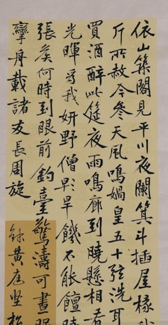 Calligraphy written in black ink on a beige paper, featuring vertical lines of Chinese characters. The characters are bold and elegantly crafted, demonstrating traditional brushwork techniques.