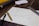 A piece of paper with a hand-drawn graph is placed on a wooden table. The graph depicts a line chart with upward trends labeled 'Sucking,' 'The Past,' and 'The Future'. Next to the paper are a black pen and a gold pen, along with a metallic ruler. In the background, partially visible are some books and sheets of paper.