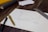 A piece of paper with a hand-drawn graph is placed on a wooden table. The graph depicts a line chart with upward trends labeled 'Sucking,' 'The Past,' and 'The Future'. Next to the paper are a black pen and a gold pen, along with a metallic ruler. In the background, partially visible are some books and sheets of paper.