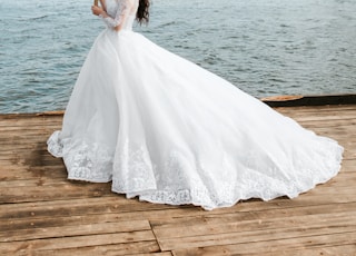 woman holding bouquet of flowers wearing wedding dress standing on dock during day