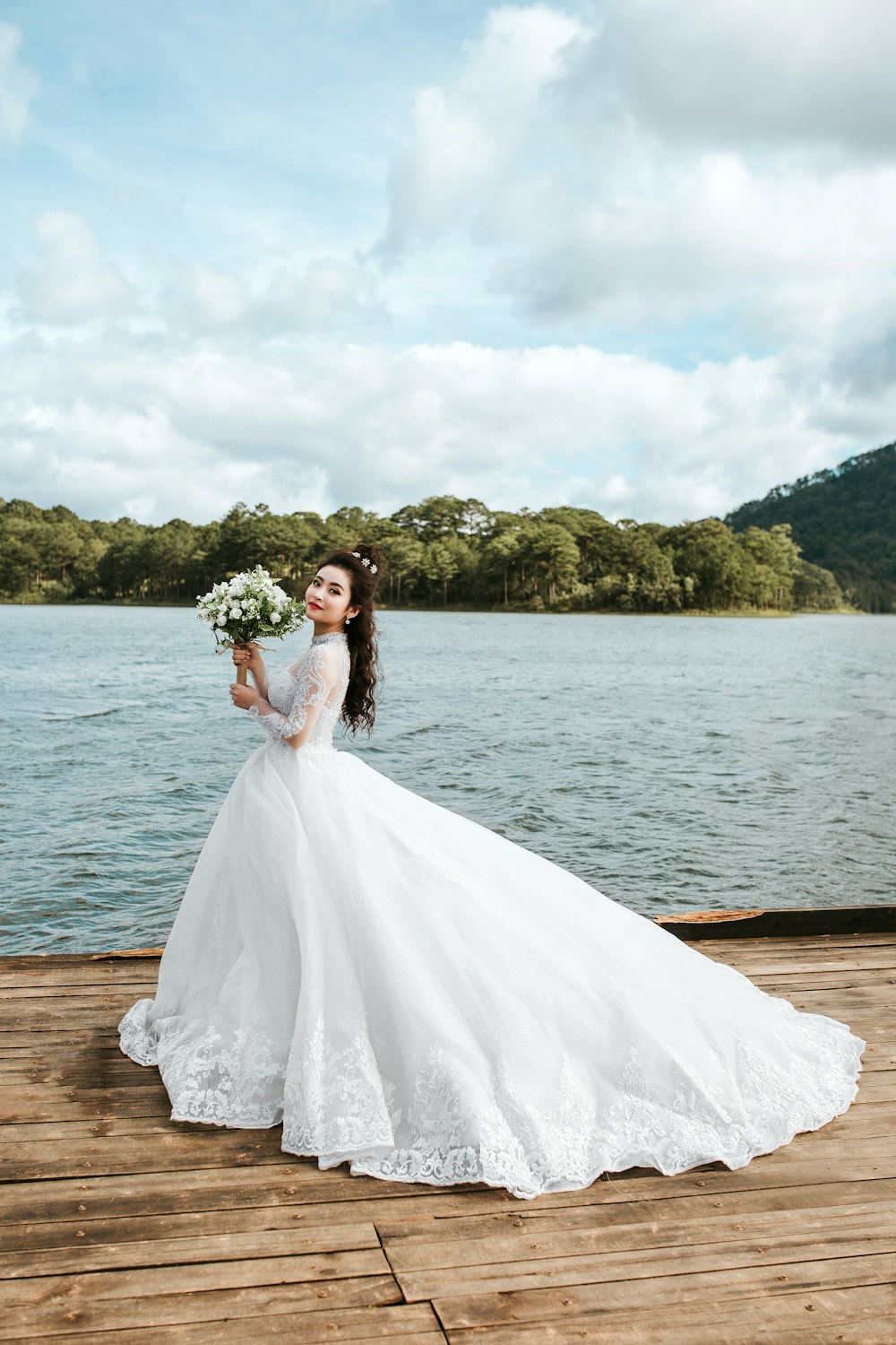 woman holding bouquet of flowers wearing wedding dress standing on dock during day