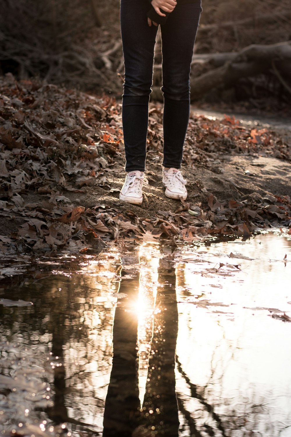 person standing near the body of water wearing black jeans during daytime