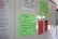 A classroom whiteboard with colorful educational posters and notes. Each poster contains scientific text, with some featuring illustrations or diagrams. Notes are written in various colors, including green, red, and pink papers pinned to the board. A hand is partially visible, suggesting interaction with the board.