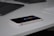 A smartphone rests on a plain white surface next to a sleek black laptop and part of a white keyboard. The smartphone's screen reflects icons and applications, indicating it is on a desk setup likely used for work or study.