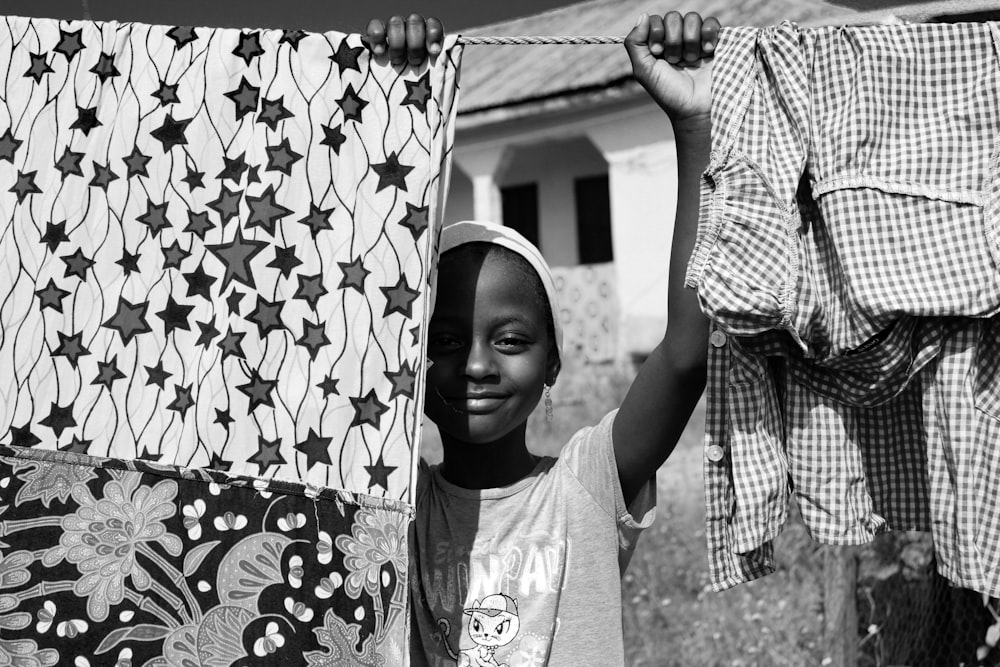 grayscale photo of boy in hat holding clothes hanger rope with clothes