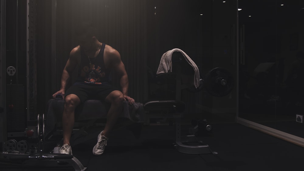 man wearing black tank top sitting on the weight bench