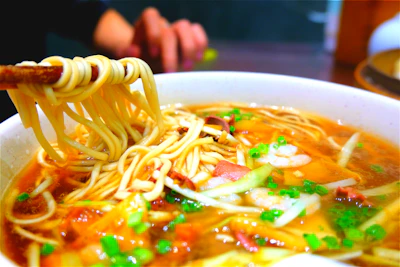 Close-up of a steaming bowl of colorful Chinese noodles with vegetables.