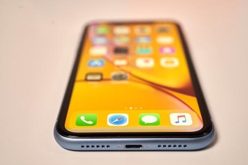 A smartphone with a bright, colorful screen displaying a variety of app icons. The perspective is from a low angle, focusing on the edge of the phone, showing its metal frame and speaker grill.