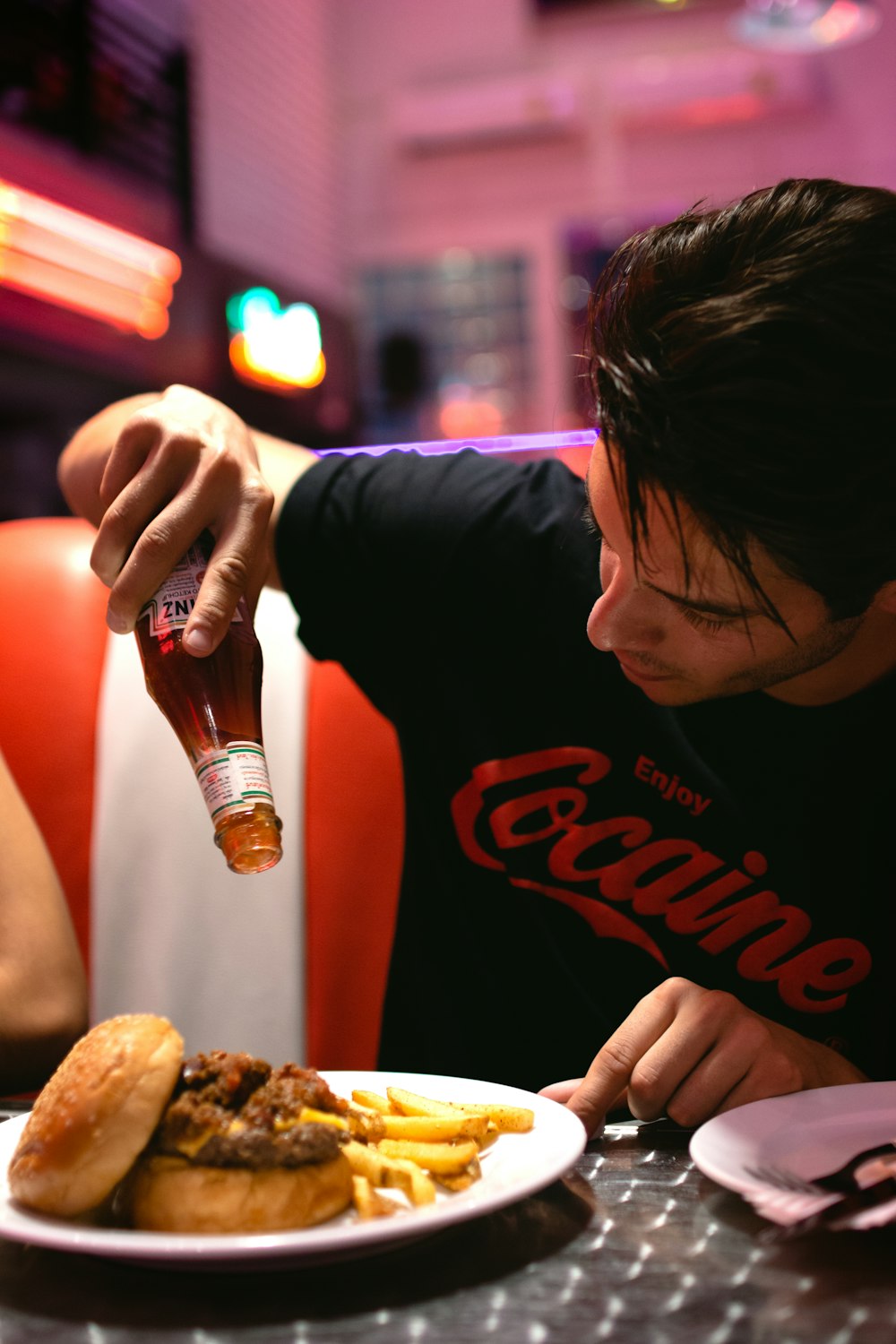 man pouring sauce on burger and fries