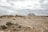 A recreational vehicle is parked on a barren, rocky landscape. The ground is covered with sparse bushes and the sky is overcast with grey clouds. The horizon appears vast and endless, contributing to a sense of solitude.