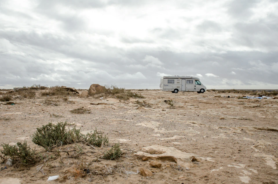 White camper van parked on desert plain, surrounded by sparse vegetation and rocky outcroppings