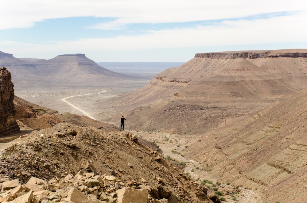 person standing at the edge of a rock mountain facing the mountains during day