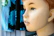 A mannequin head with detailed facial features and brown hair is in profile view. The background consists of out-of-focus fabric or clothing with blue and black patterns.