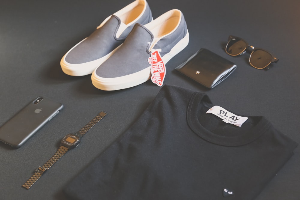camicia Play nera piegata accanto a iPhone X, orologio digitale e scarpe da ginnastica