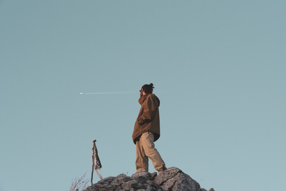 man in brown jacket standing on rock hill