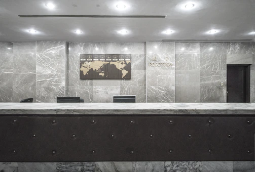 A professional concierge warmly greeting a client at a sleek modern reception desk.