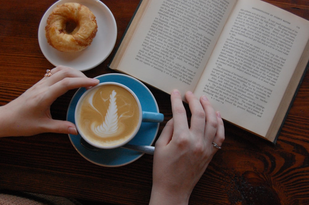 person holding blue ceramic teacup beside the book