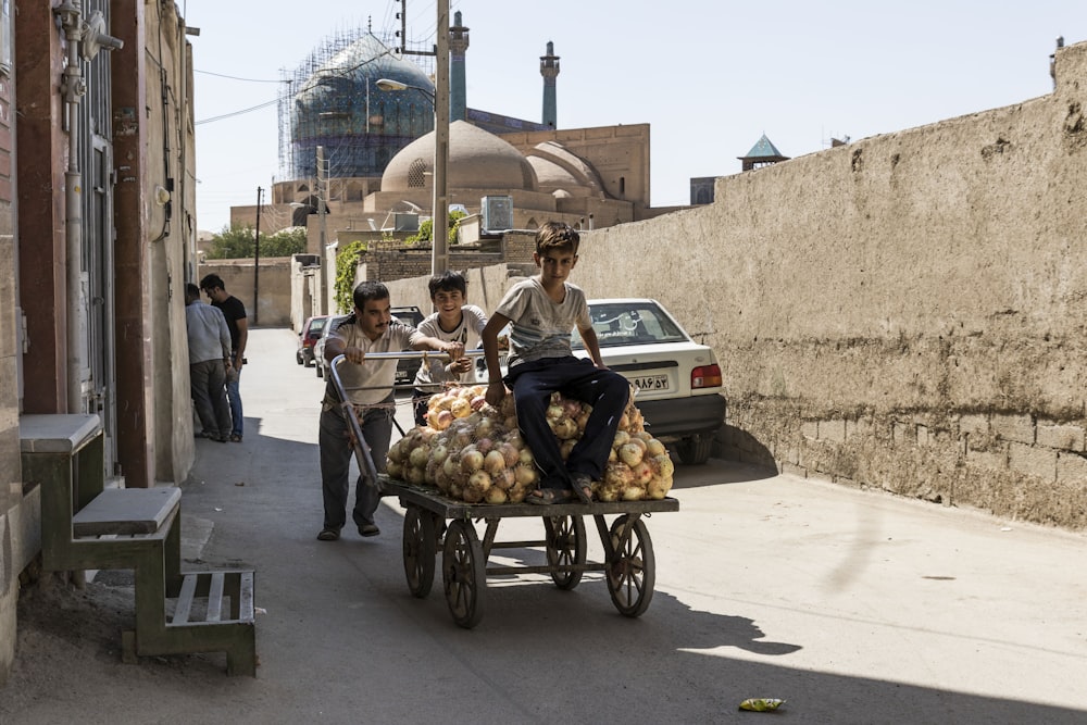 boy riding on cart with two boys pushing during daytime