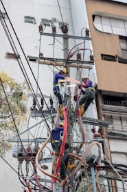 three people climbing on electric post