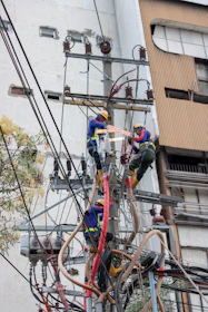 three people climbing on electric post