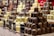 Several stacks of assorted chocolate-covered confections are displayed on a checkered tablecloth. The treats vary in flavors, indicated by small signs labeled gingerbread, white coconut, milky coconut, and caramel. Each stack features chocolates drizzled or sprinkled with toppings, creating an appealing and abundant display of sweets.