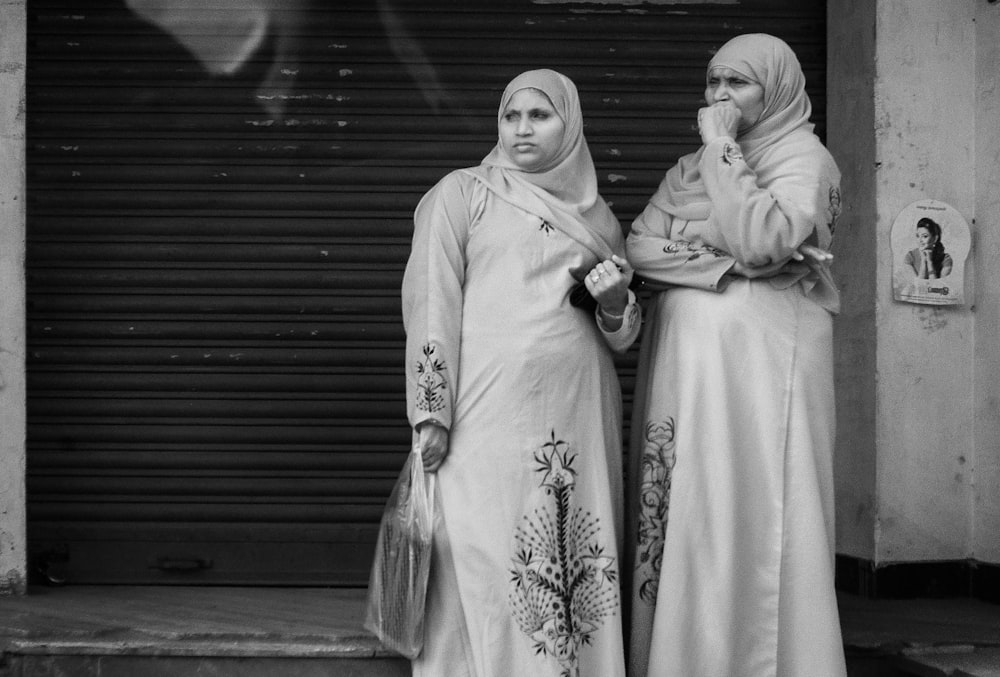 grayscale photography of two women standing near roll-up door