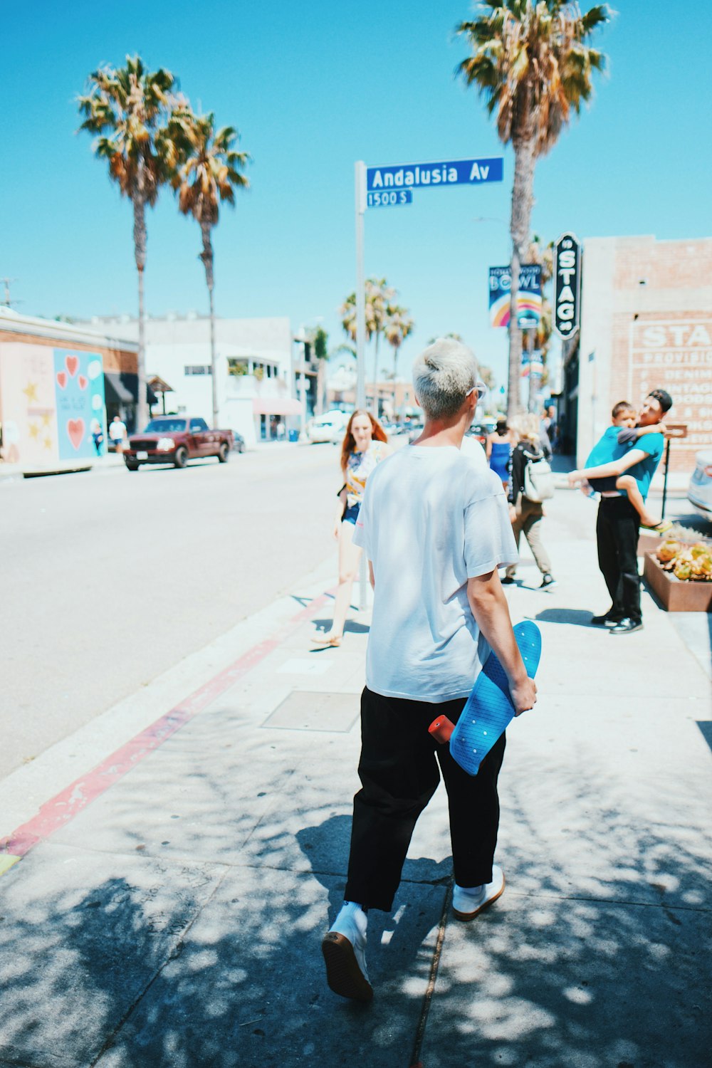 Mann geht mit blauem Longboard in der Hand