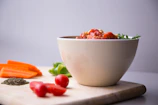 A rustic ceramic bowl filled with vibrant vegetable ratatouille, garnished with basil.