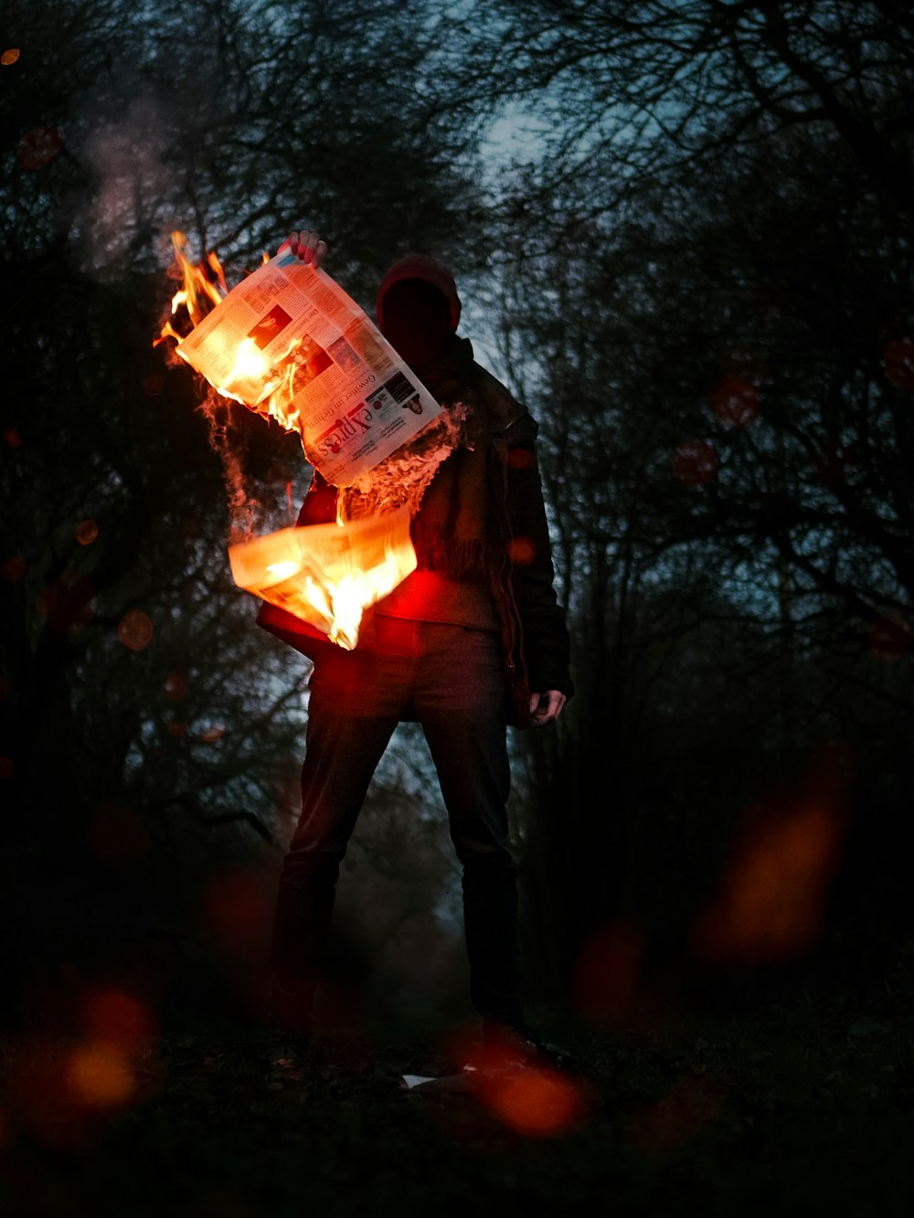 person holding burning newspapers while standing near trees