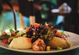 A plate of assorted Mediterranean dips including hummus, served with fresh greens, diced tomatoes, and other colorful vegetables. The arrangement is artfully presented with focus on texture and vibrant colors.