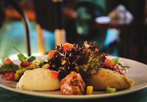 A plate of assorted Mediterranean dips including hummus, served with fresh greens, diced tomatoes, and other colorful vegetables. The arrangement is artfully presented with focus on texture and vibrant colors.