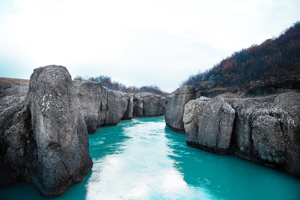 river in the middle of grey rocks under white clouds