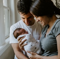 woman holding baby beside man smiling