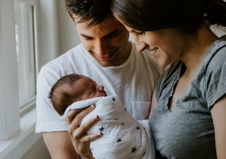 woman holding baby beside man smiling