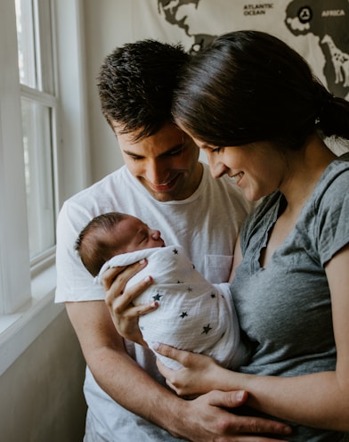 woman holding baby beside man smiling