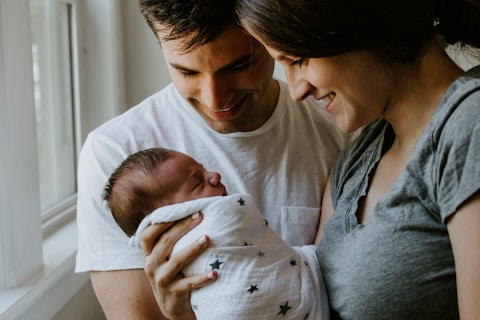 woman holding baby beside man smiling