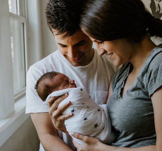 woman holding baby beside man smiling