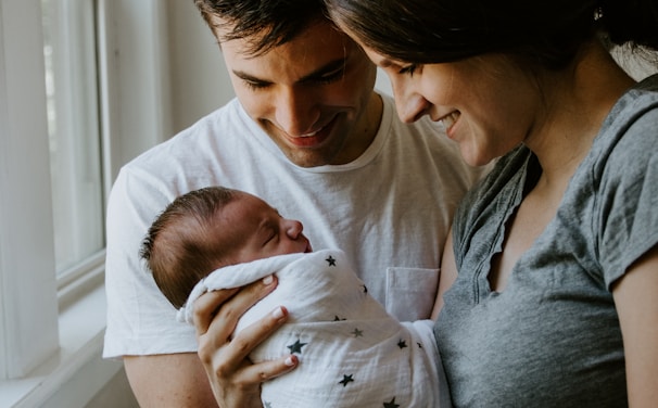 woman holding baby beside man smiling