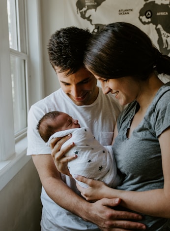 woman holding baby beside man smiling