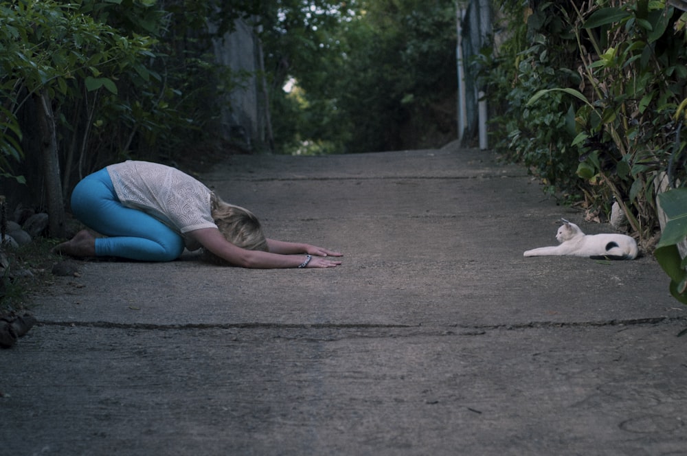 mujer arrodillada frente a un gato que yace en el suelo