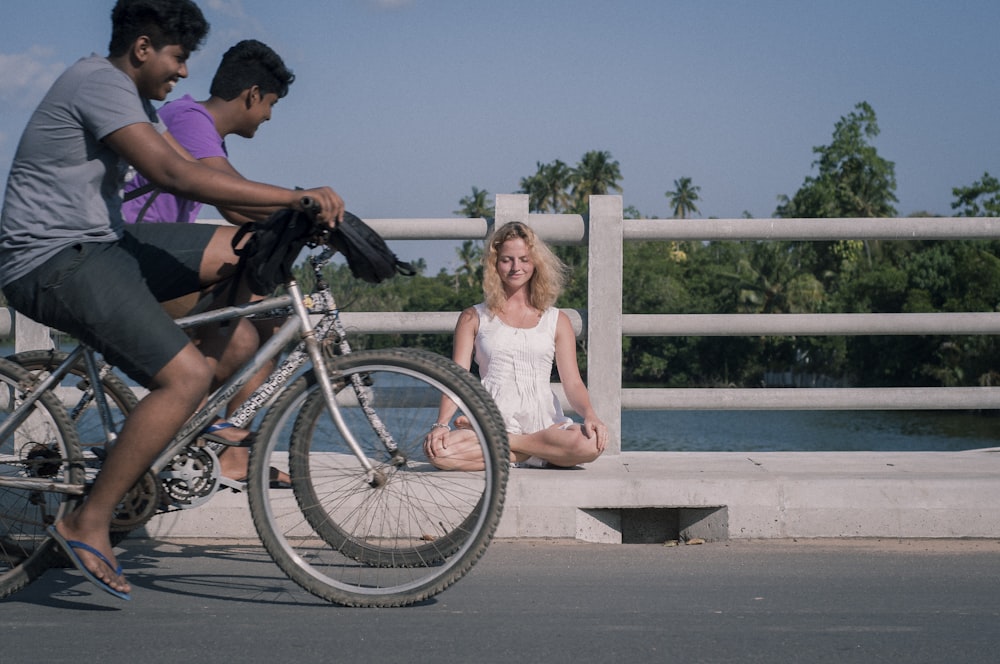 woman sits on curb with two men on bikes passing