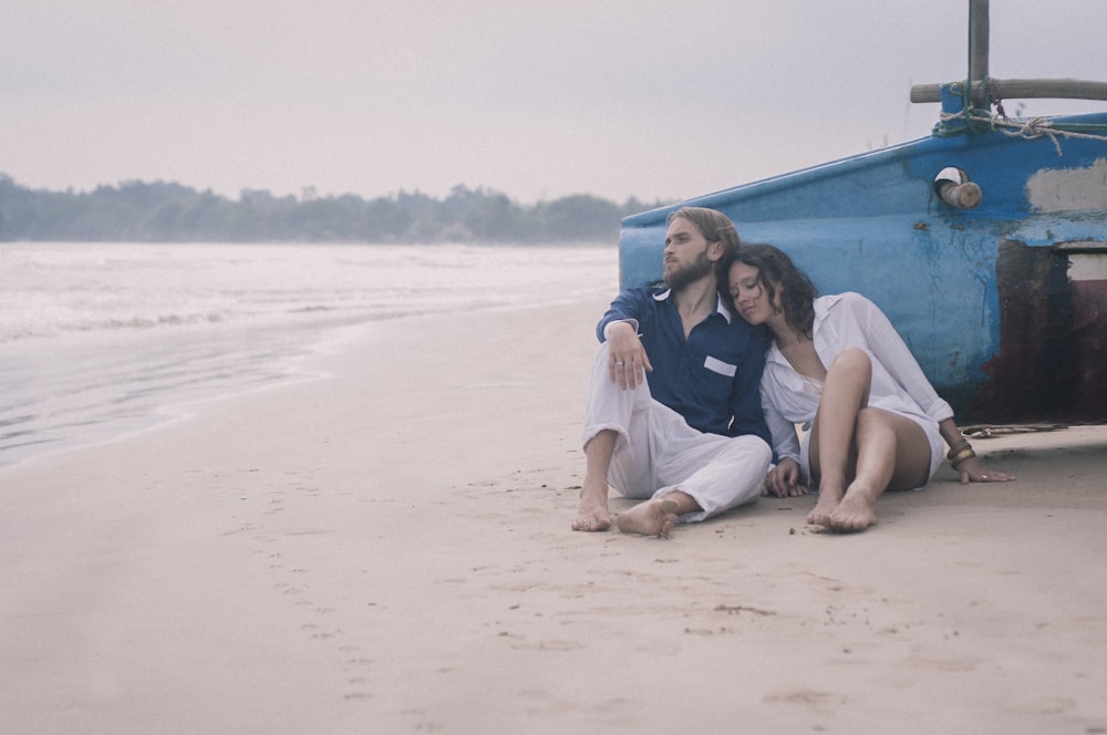man and woman sits on beach sand