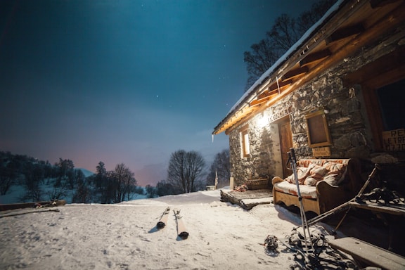 A cozy mountain cabin at sunrise with fresh snow and ski gear leaning against the porch.