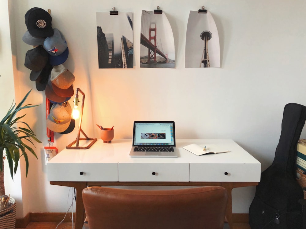 open laptop on table beside guitar bag and hanging hats