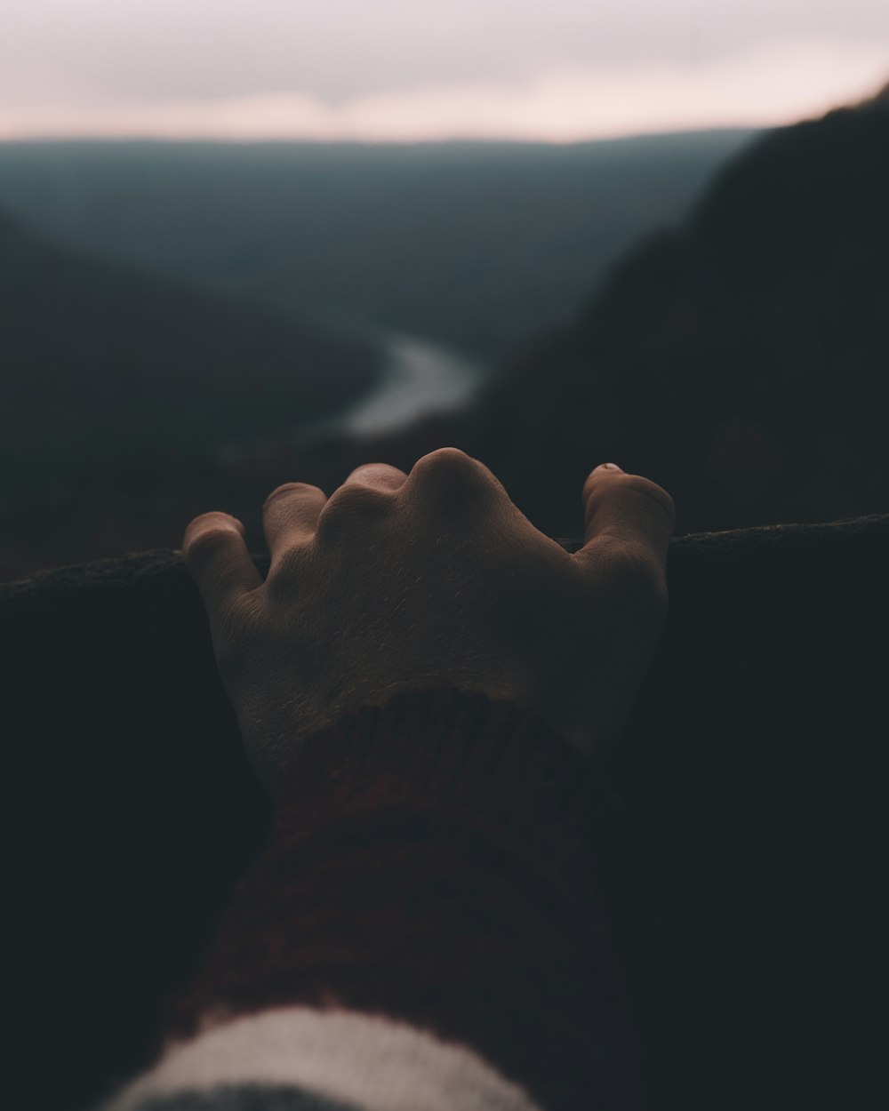 person's hand holding railings overlooking winding river