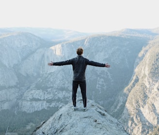 man opening his arms wide open on snow covered cliff with view of mountains during daytime